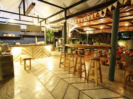 Un área de bar interior con taburetes de madera, una barra y piso de baldosas.