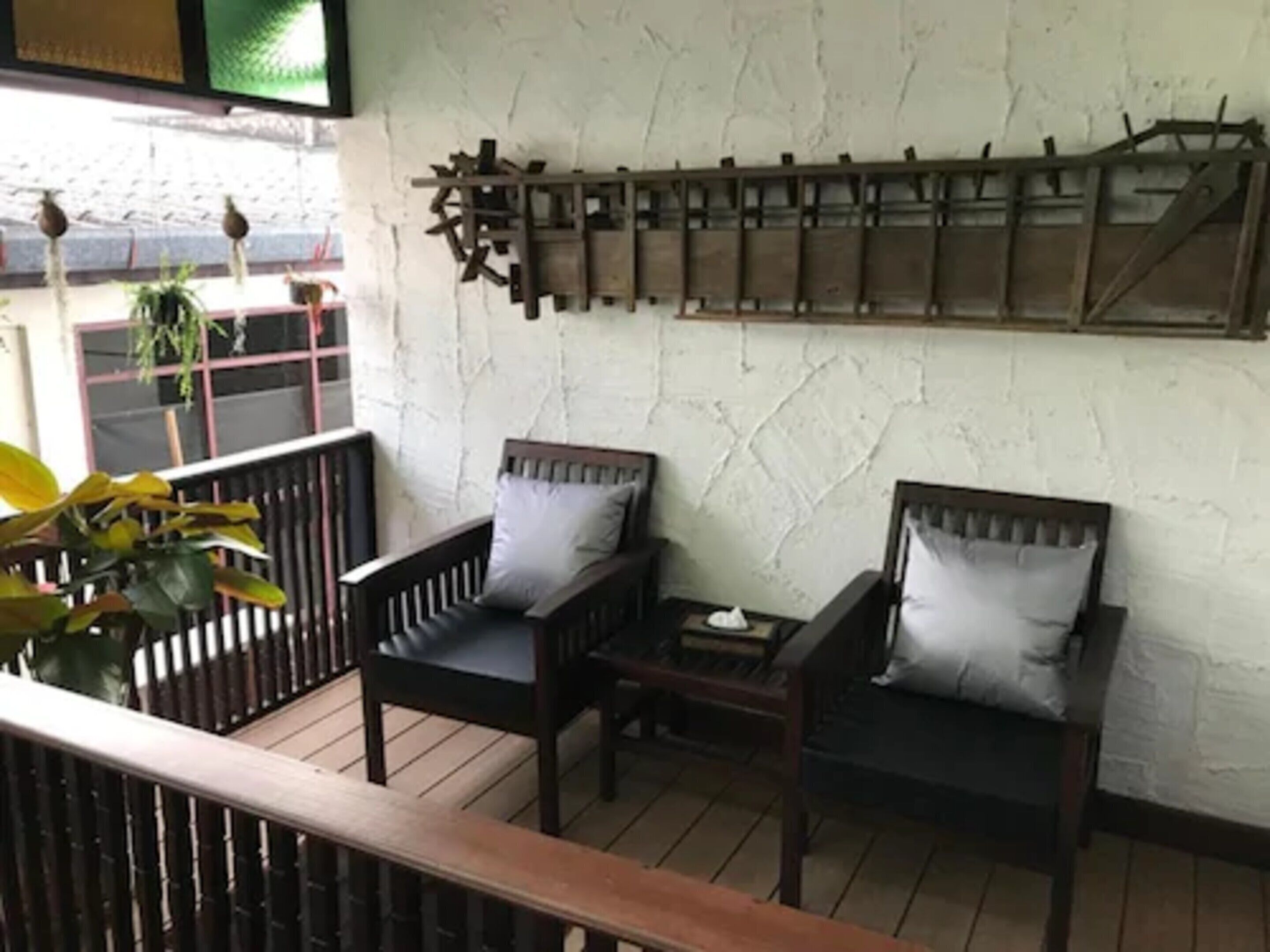 Una terraza de madera con dos sillas y una mesita, una pared blanca con textura y un estante de madera encima.