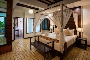 A bedroom with a four-poster bed, a bedside table, a nightstand, and a view of a balcony.