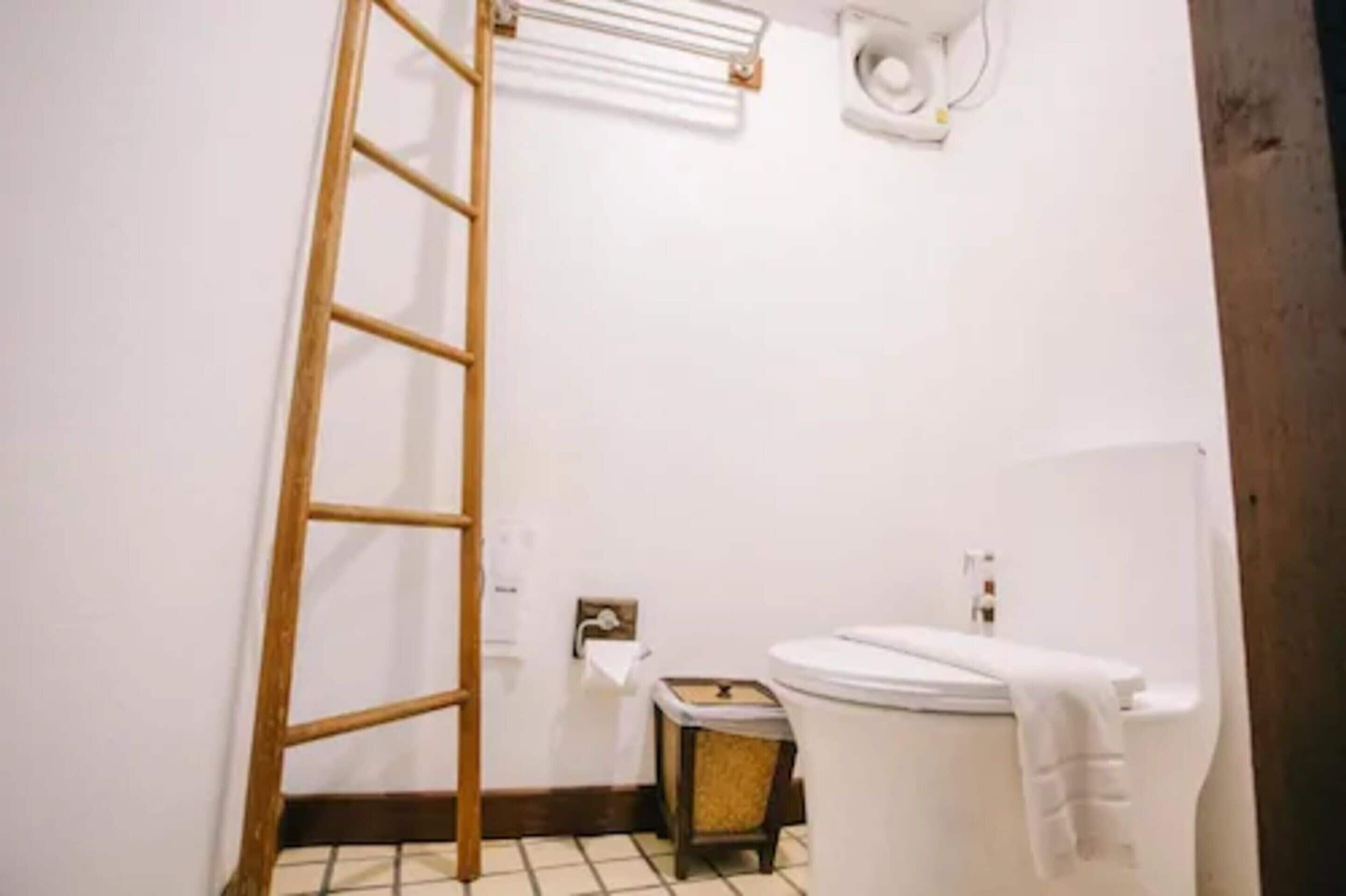 A bathroom with a wooden ladder, a toilet, a sink, and a towel rack.