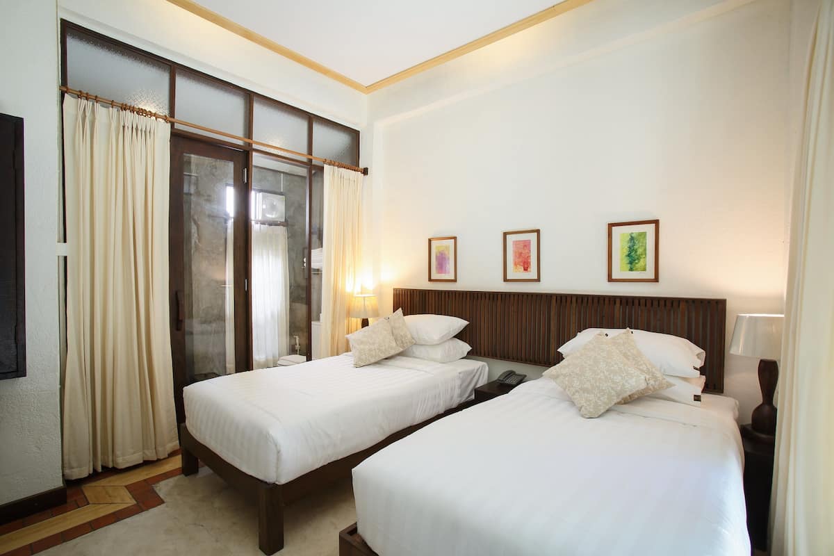 Een hotelkamer met twee bedden, een groot raam met gordijnen, een houten hoofdbord en drie ingelijste foto's aan de muur.