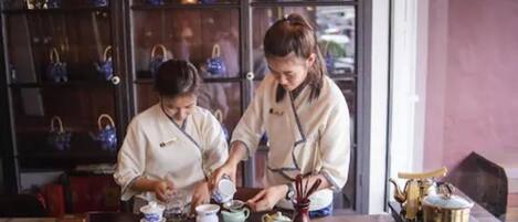 Two individuals serving tea at a table with multiple teapots and cups.