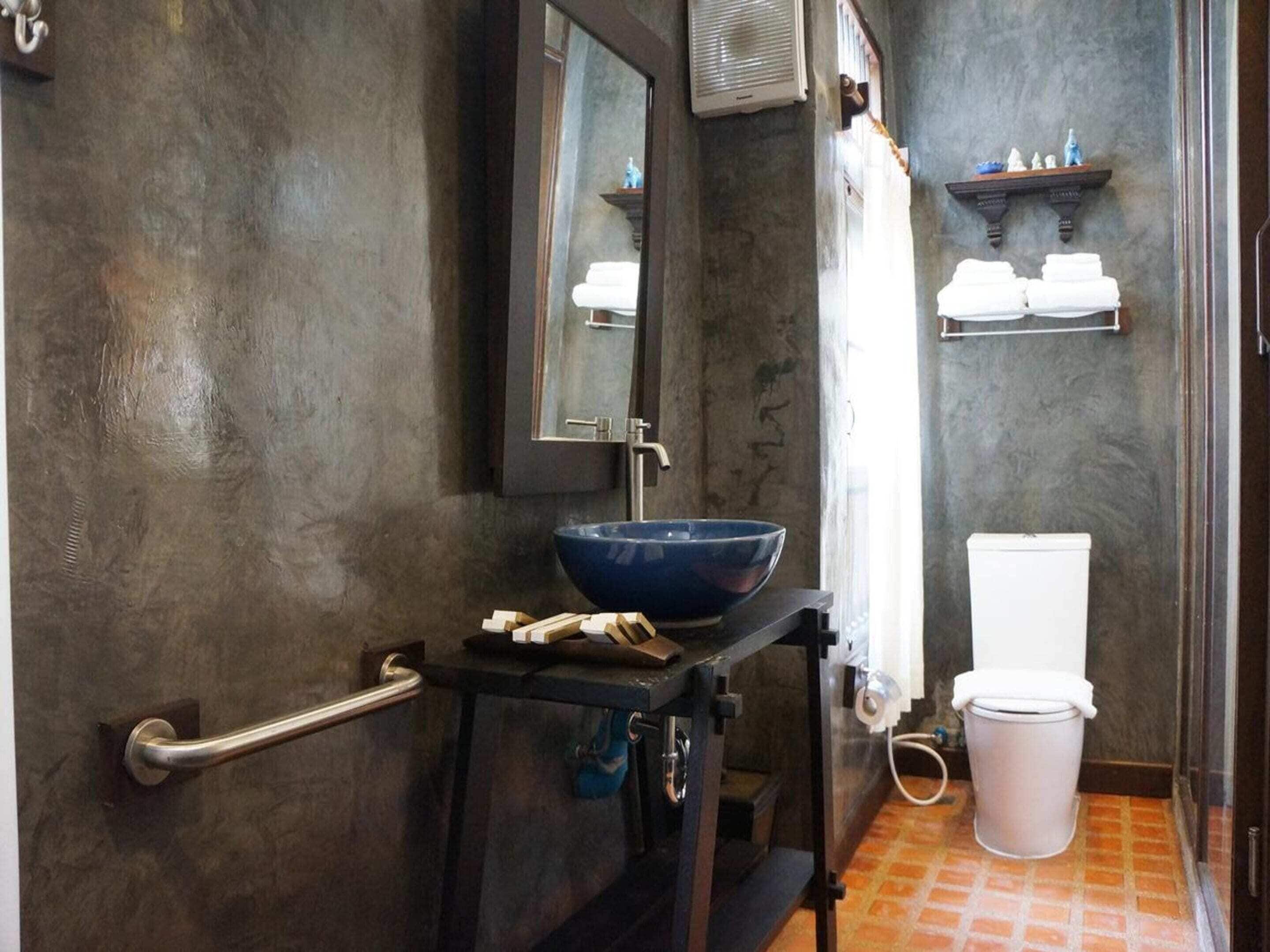 A bathroom with a large blue basin, a white toilet, a towel rack, and a mirror.