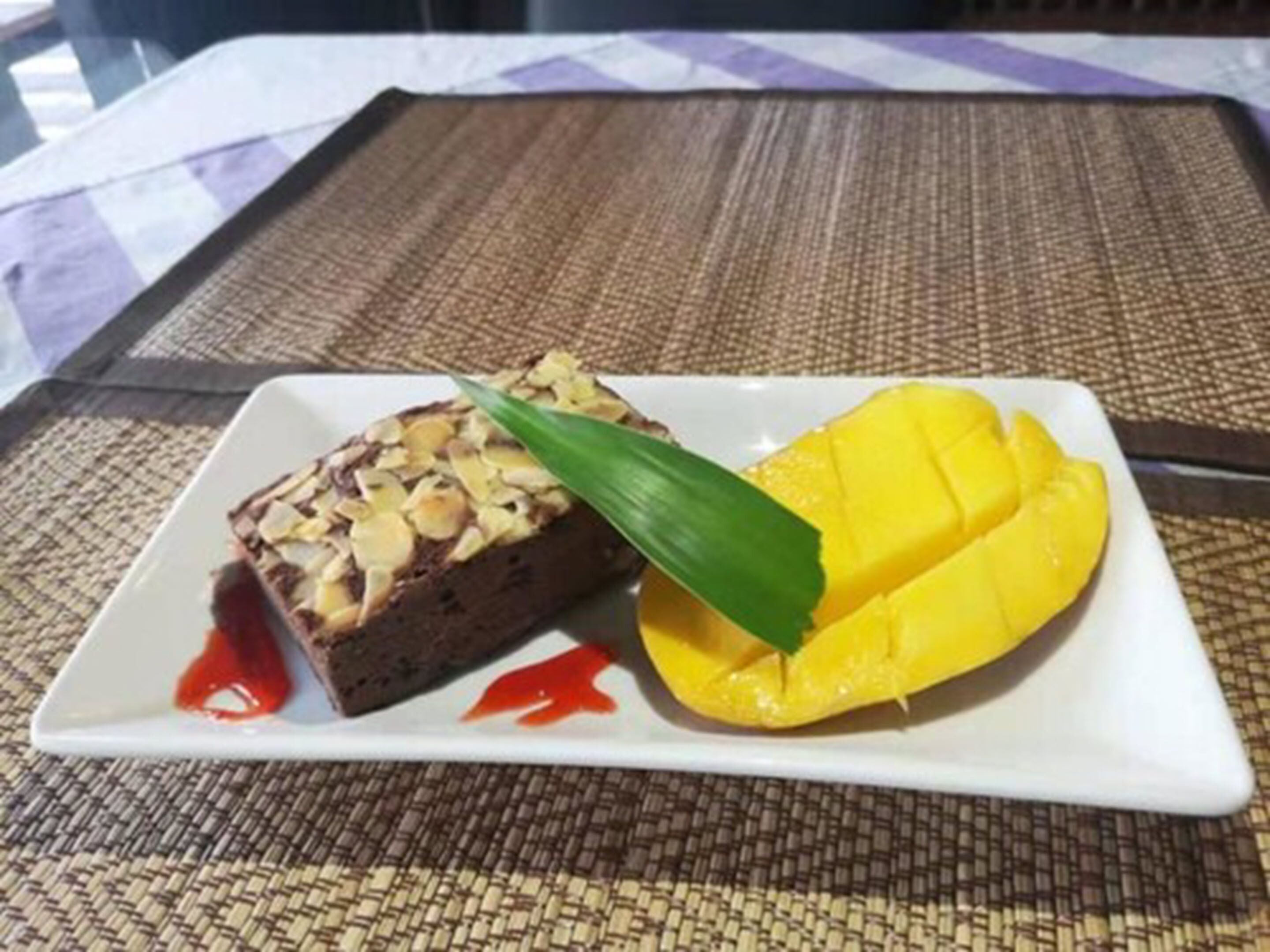 A dessert plate with a slice of cake topped with almonds and a mango on the side.