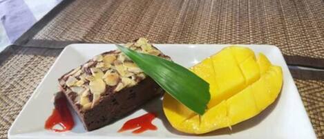 A dessert plate with a slice of cake topped with almonds and a mango on the side.