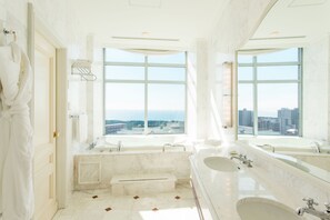 A luxurious bathroom with large windows, a bathtub, and two sinks.