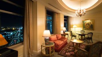 A hotel room with a large window offering a city view, a red sofa, a round table, and a chandelier.