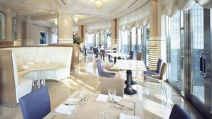 Un restaurante amplio y luminoso, con techos altos, elegantes candelabros y grandes ventanales que ofrecen vistas del paisaje urbano.