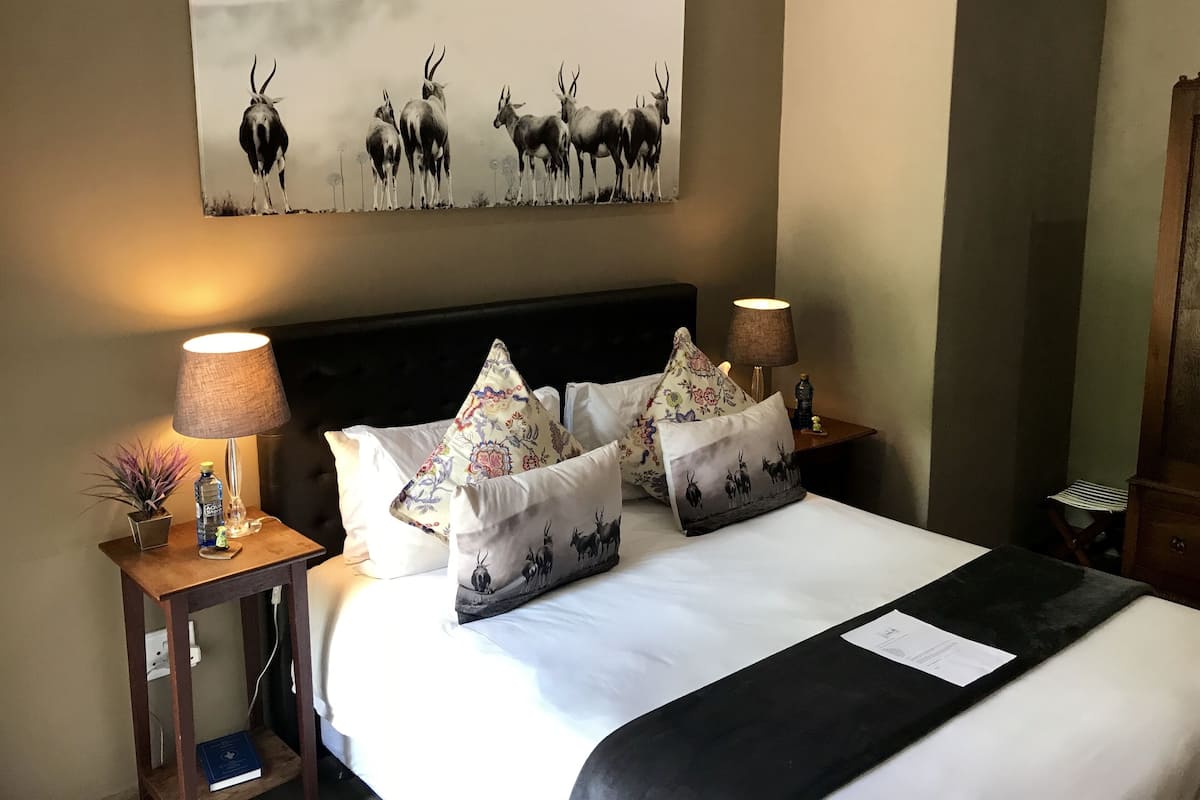 Una cama bien hecha con almohadillas estampadas, cabecera y un cuadro colgado en la pared con antílopes.