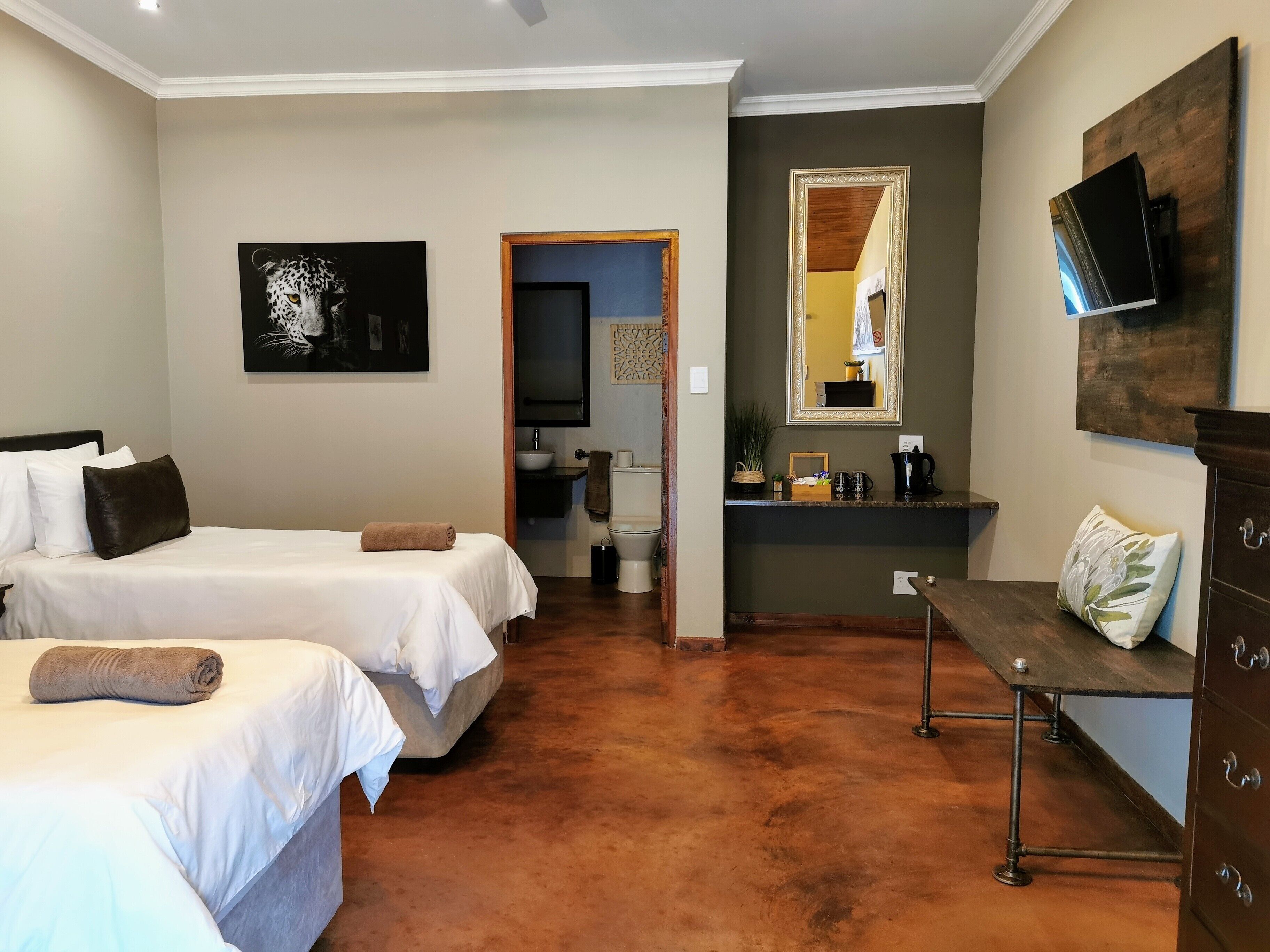 A hotel room with two beds, a bathroom, a small sitting area, and a TV mounted on the wall.