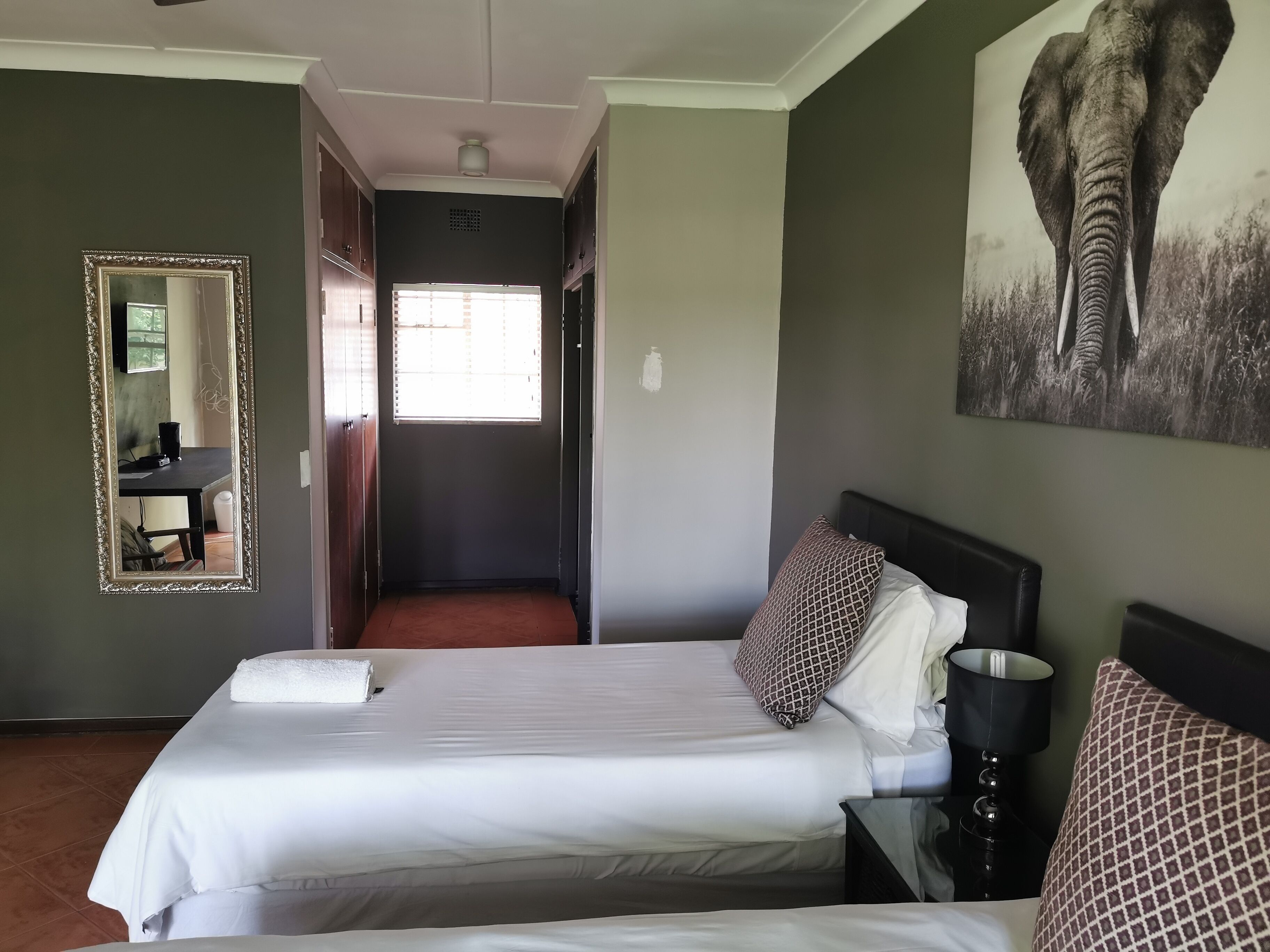 Habitación de hotel con una cama grande, una mesita de noche, un espejo e imagen de un elefante colgada en la pared.