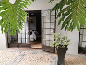 Een kamer met een bed, een potplant en een raam met een metalen traliewerk.