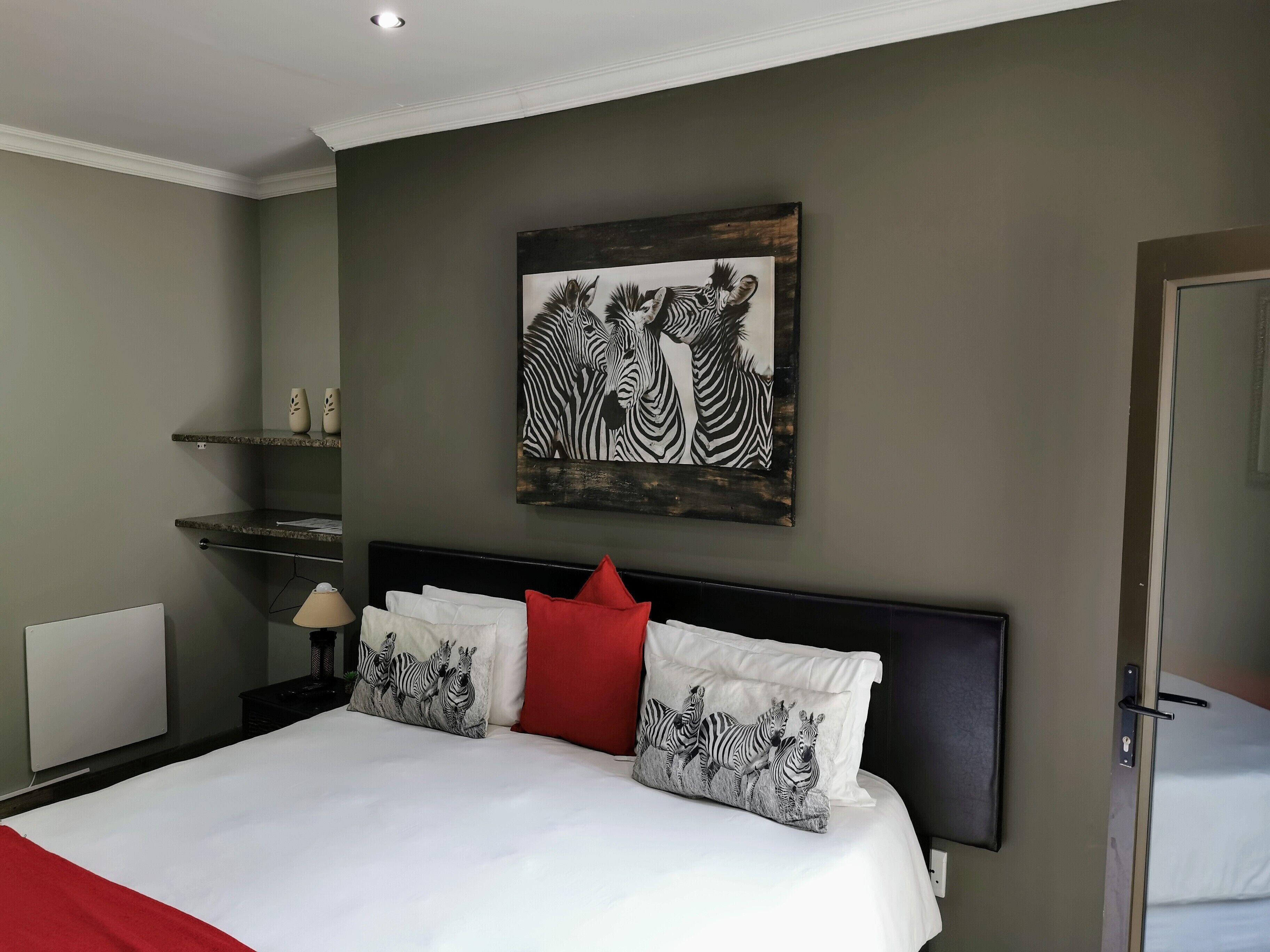 Quarto com uma cama grande, almofadas com tema de zebra, uma pintura de zebra na parede e uma pequena prateleira com objetos decorativos.