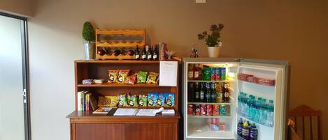 Una habitación con un armario de madera que contiene aperitivos, un libro de visitas y una pequeña planta en maceta. También se puede ver un refrigerador lleno de bebidas y aperitivos.
