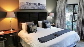 Un letto rifatto con cura, caratterizzato da una palette di colori bianco e grigio, affiancato da due comodini con lampade, una testiera con pannello decorativo e un grande quadro sopra il letto.