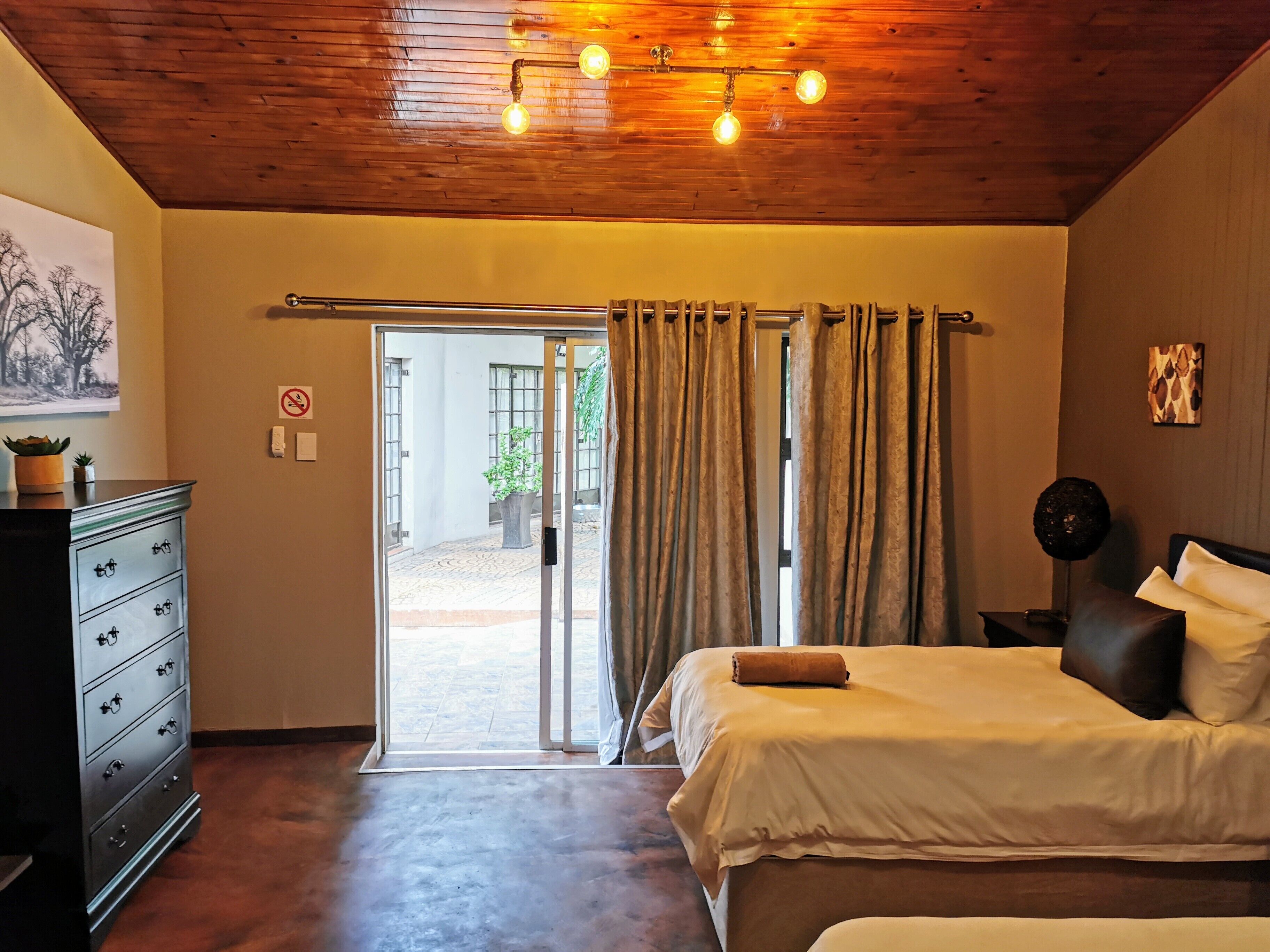 Un dormitorio con cama, cómoda, lámpara de techo y puerta corrediza de vidrio que da a un espacio exterior.