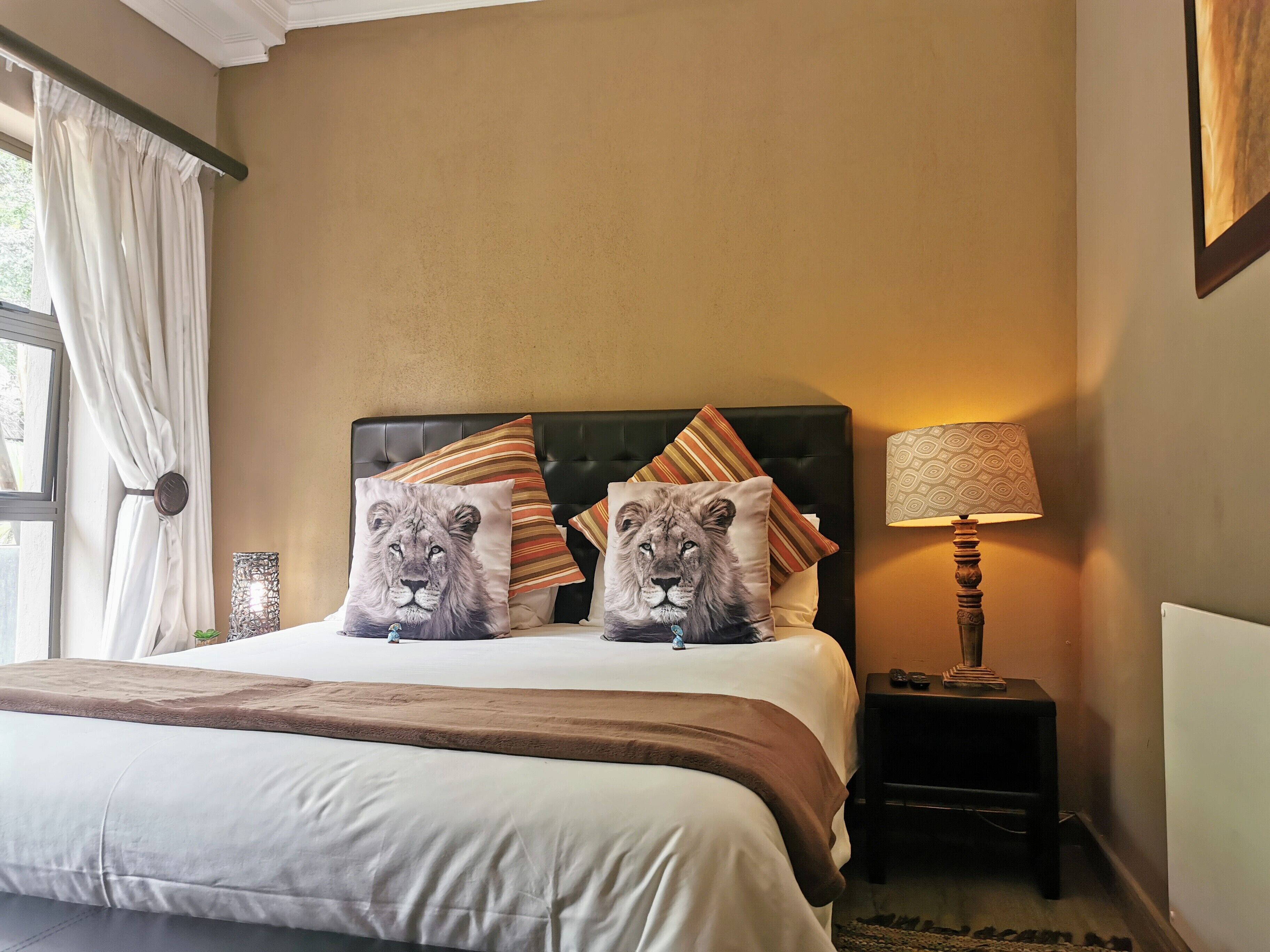 A bedroom with a bed, two pillows with lion prints, a bedside lamp, and a nightstand.