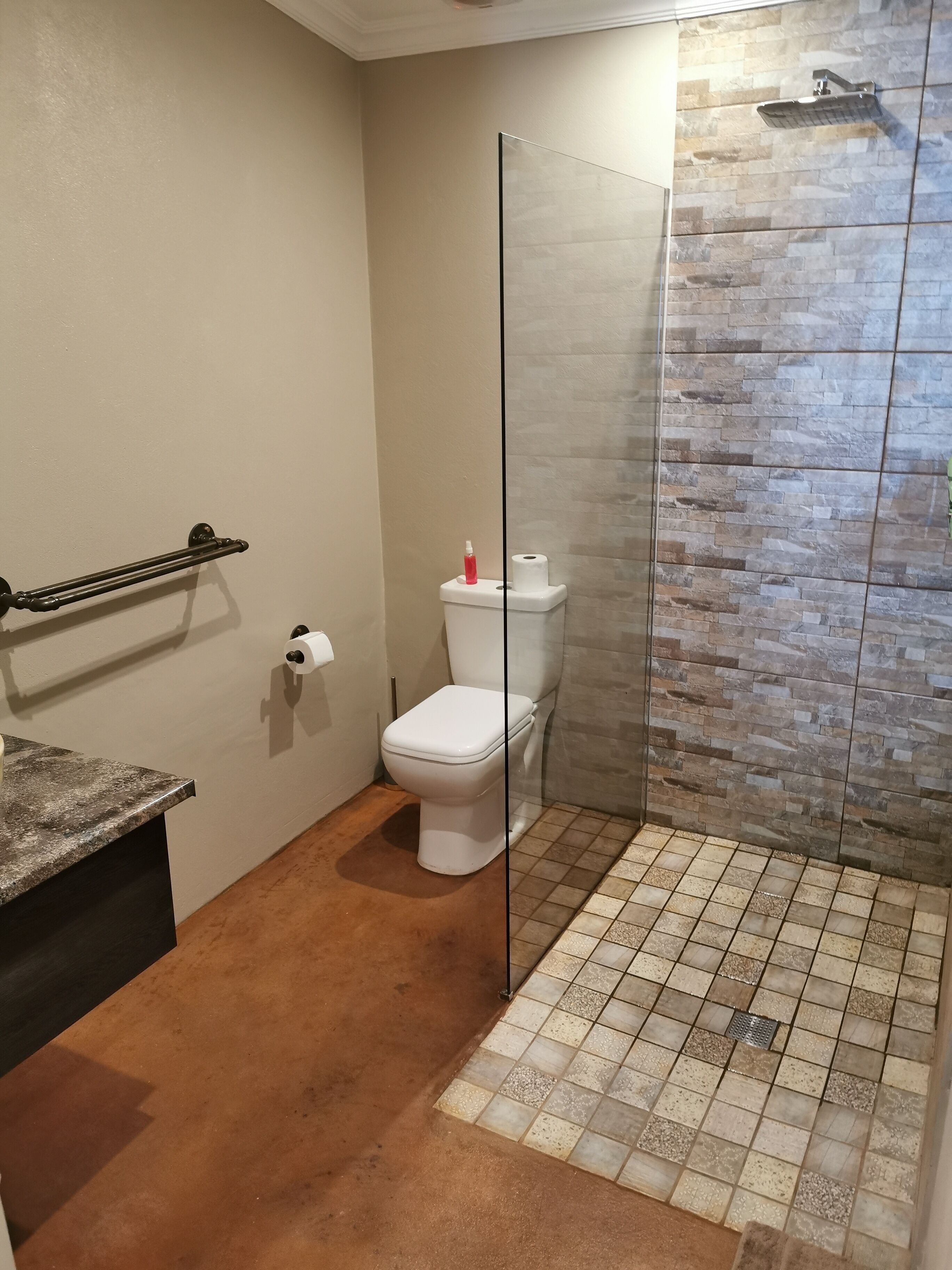 A bathroom with a toilet, a shower enclosure, a towel rack, and a marble countertop.