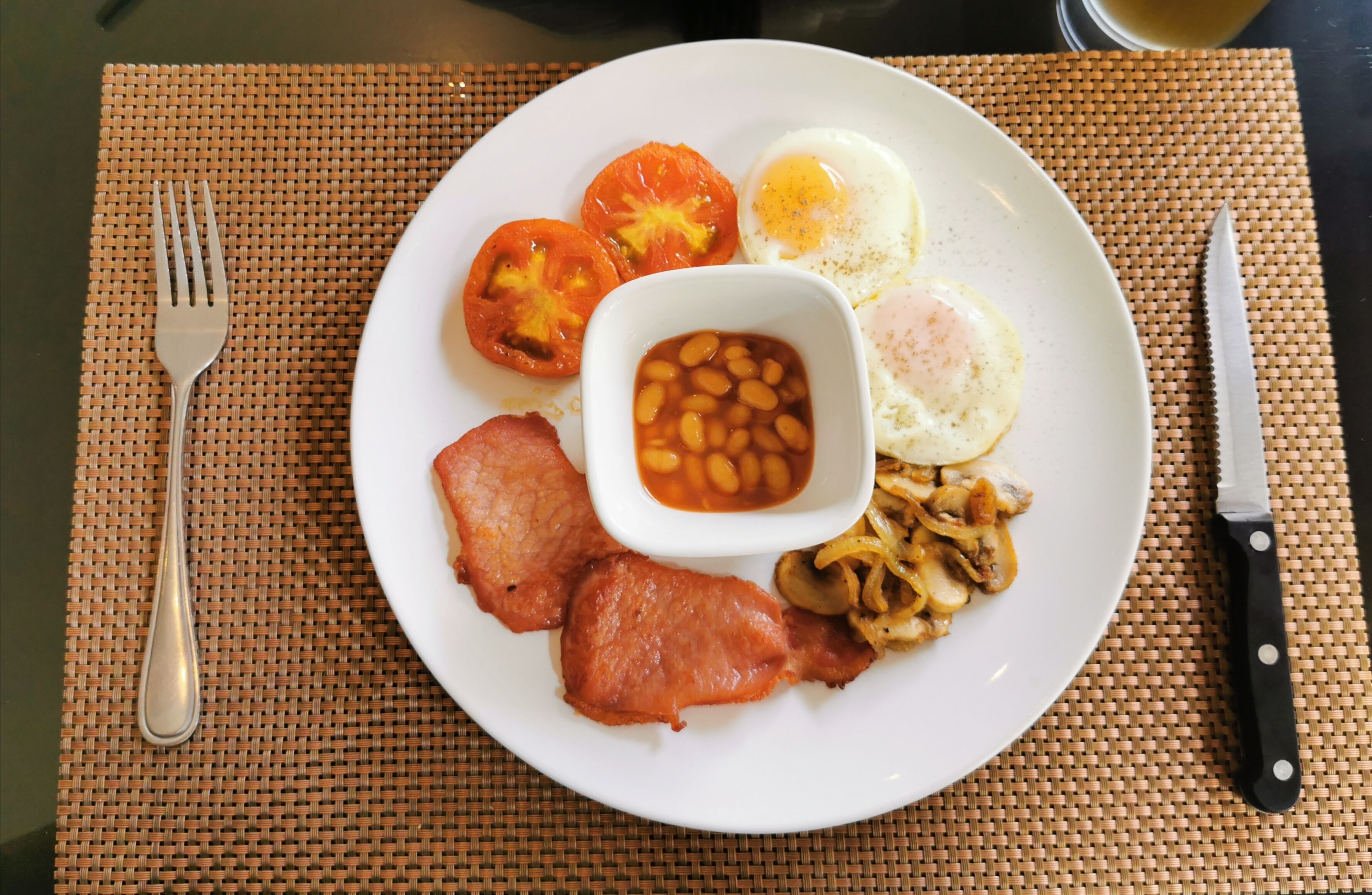 A plate of food including eggs, beans, tomatoes, bacon, and mushrooms.