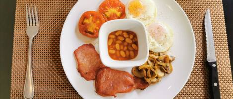 Une assiette contenant des œufs, des haricots, des tomates, du bacon et des champignons.