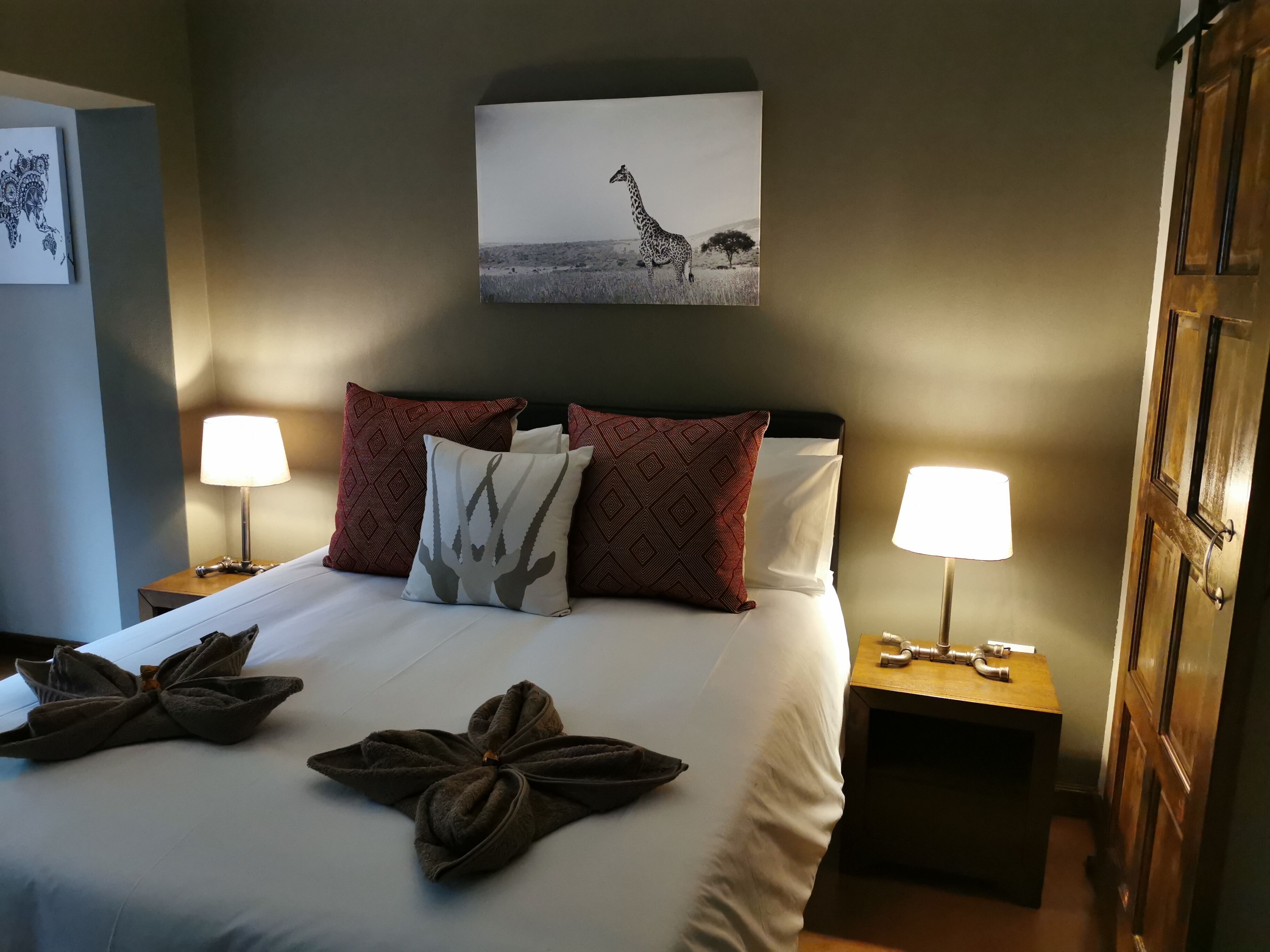 A neatly made bed with a giraffe picture above it, two nightstands with lamps, and a wooden door.