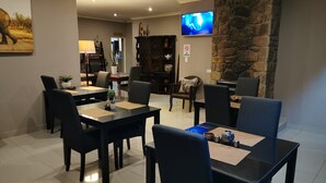 Un'area pranzo con tavoli e sedie neri, un televisore fissato alla parete e una parete decorata in pietra.