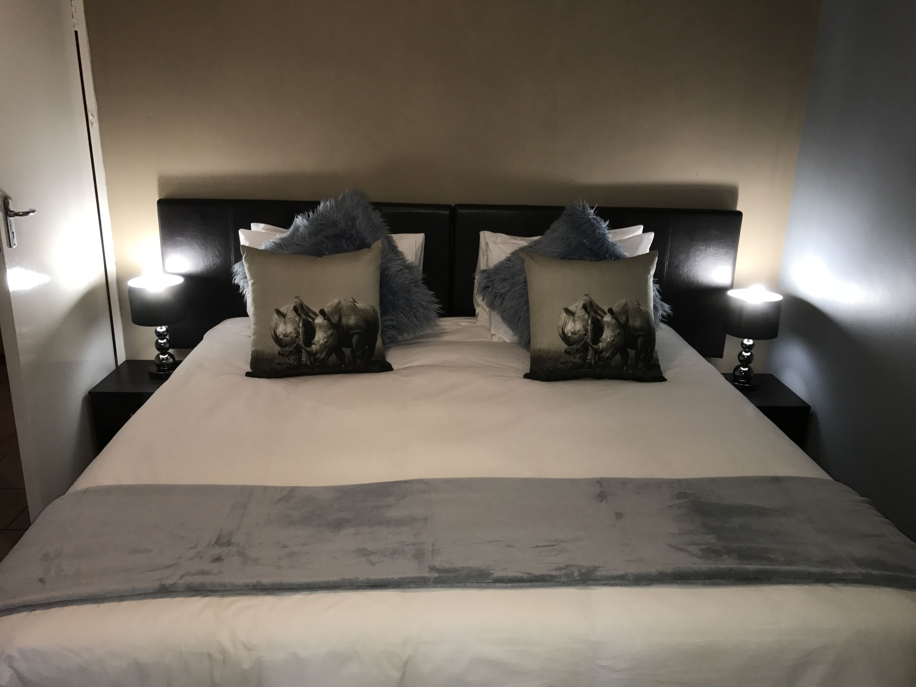 A neatly made bed with two decorative pillows featuring rhinoceros prints, flanked by two bedside lamps on black nightstands.