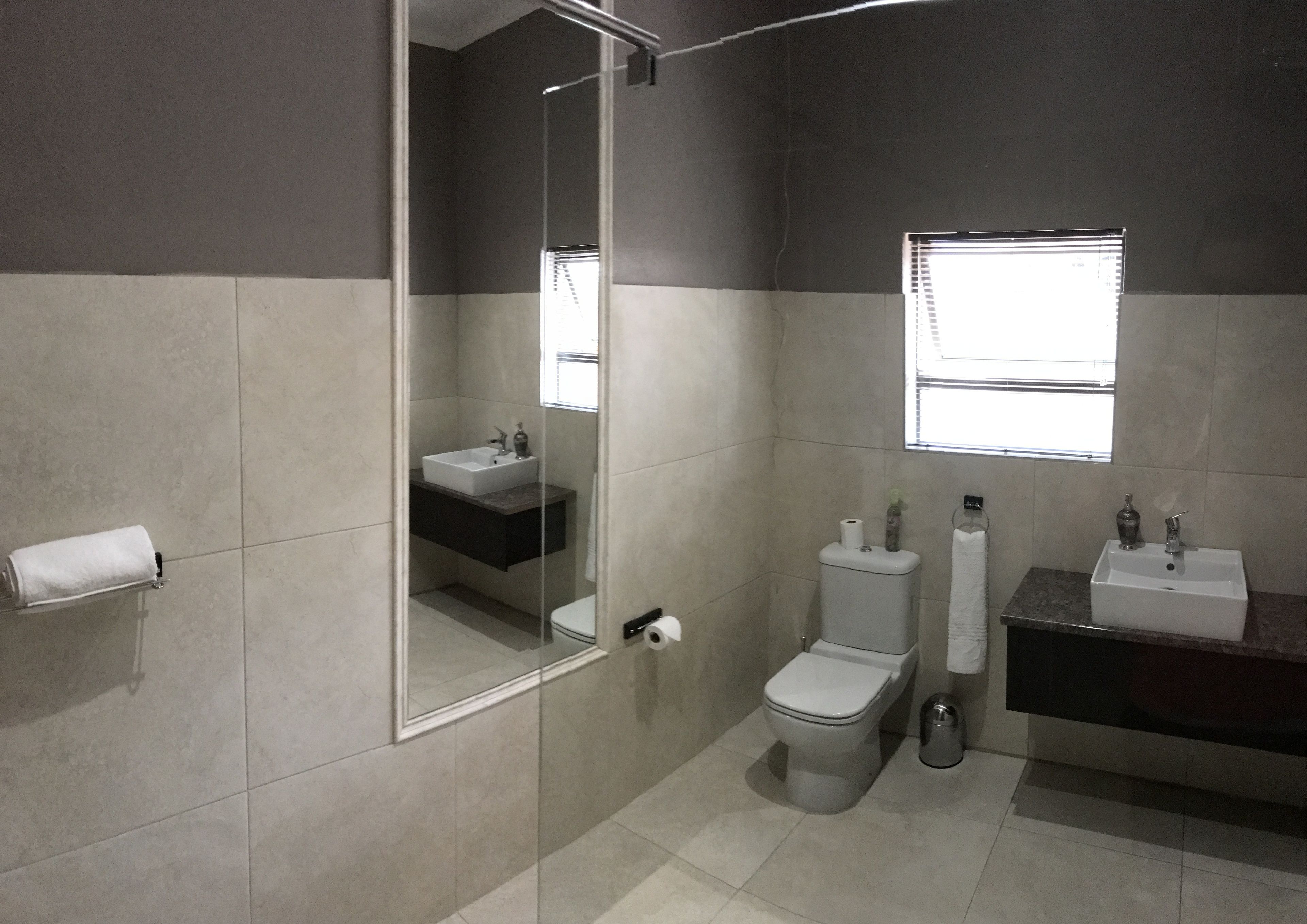 A modern bathroom with a glass shower enclosure, a toilet, a sink, and a window providing natural light.