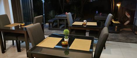 Un área de comedor al aire libre con mesas, sillas, sombrillas y una pequeña maceta.