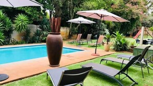 Area piscina con lettini e ombrelloni, circondata da vegetazione e un vaso di grandi dimensioni.