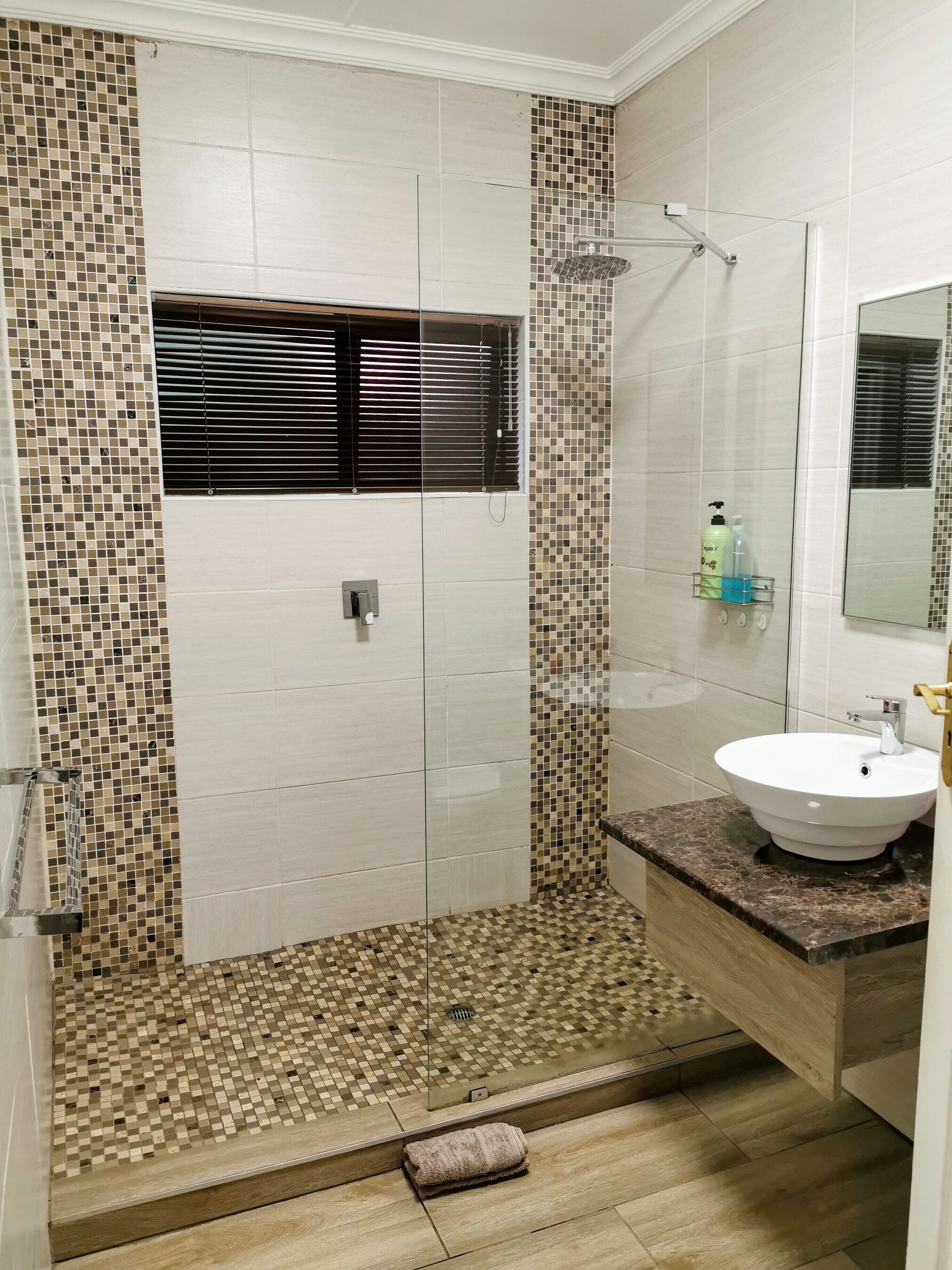 A bathroom with a shower, tiled walls, a sink, and a mirror.