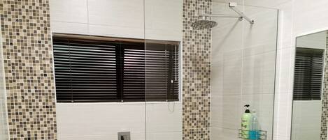 A bathroom with a shower, tiled walls, a sink, and a mirror.