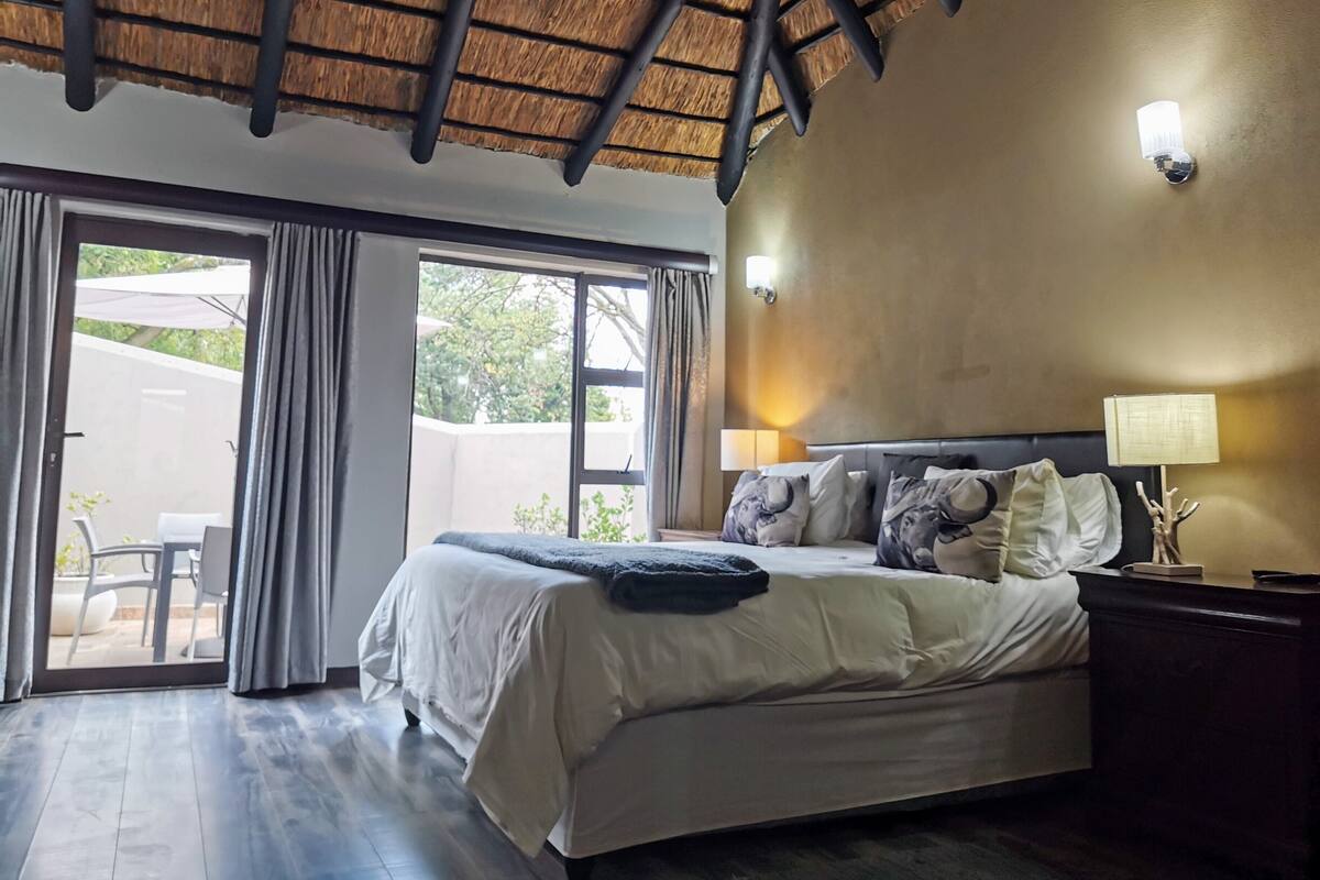 Un dormitorio con cama, mesita de noche, lámpara y vistas al exterior.