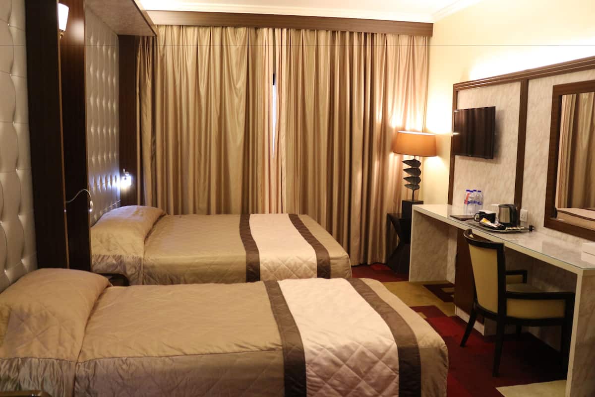 Hotellihuone, jossa on kaksi sänkyä, työpöytä, tuoli, televisio ja ikkuna, jossa on verhot.