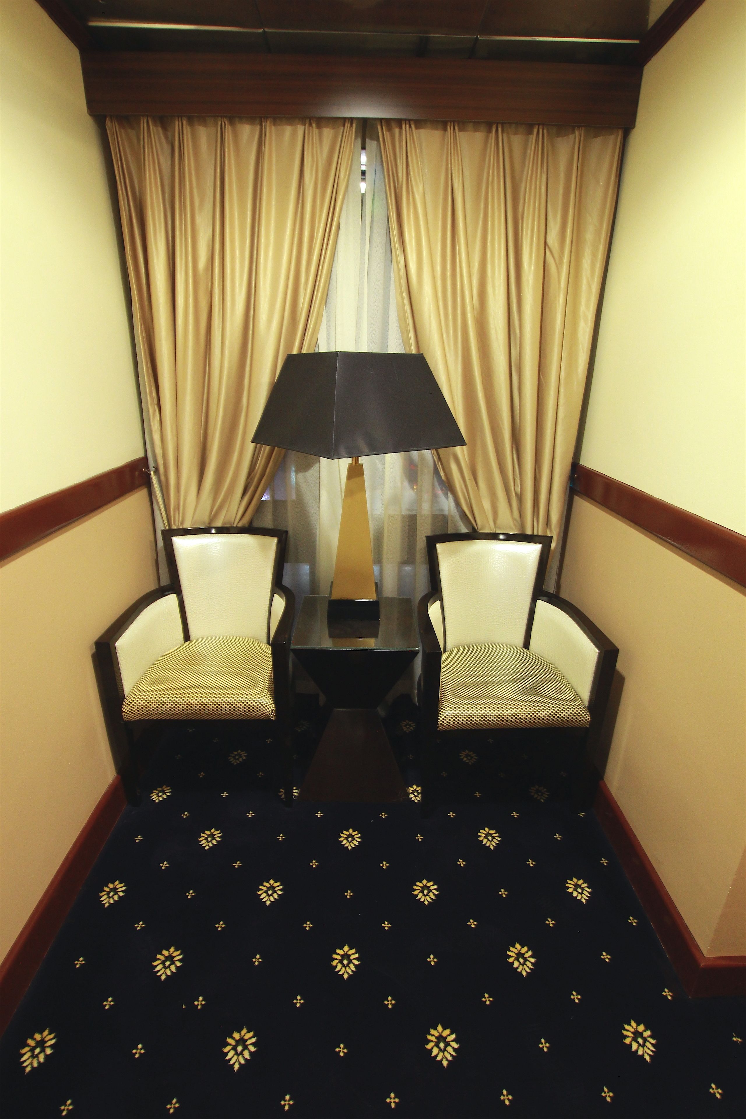 A hotel room with two chairs, a small table, and a lamp.