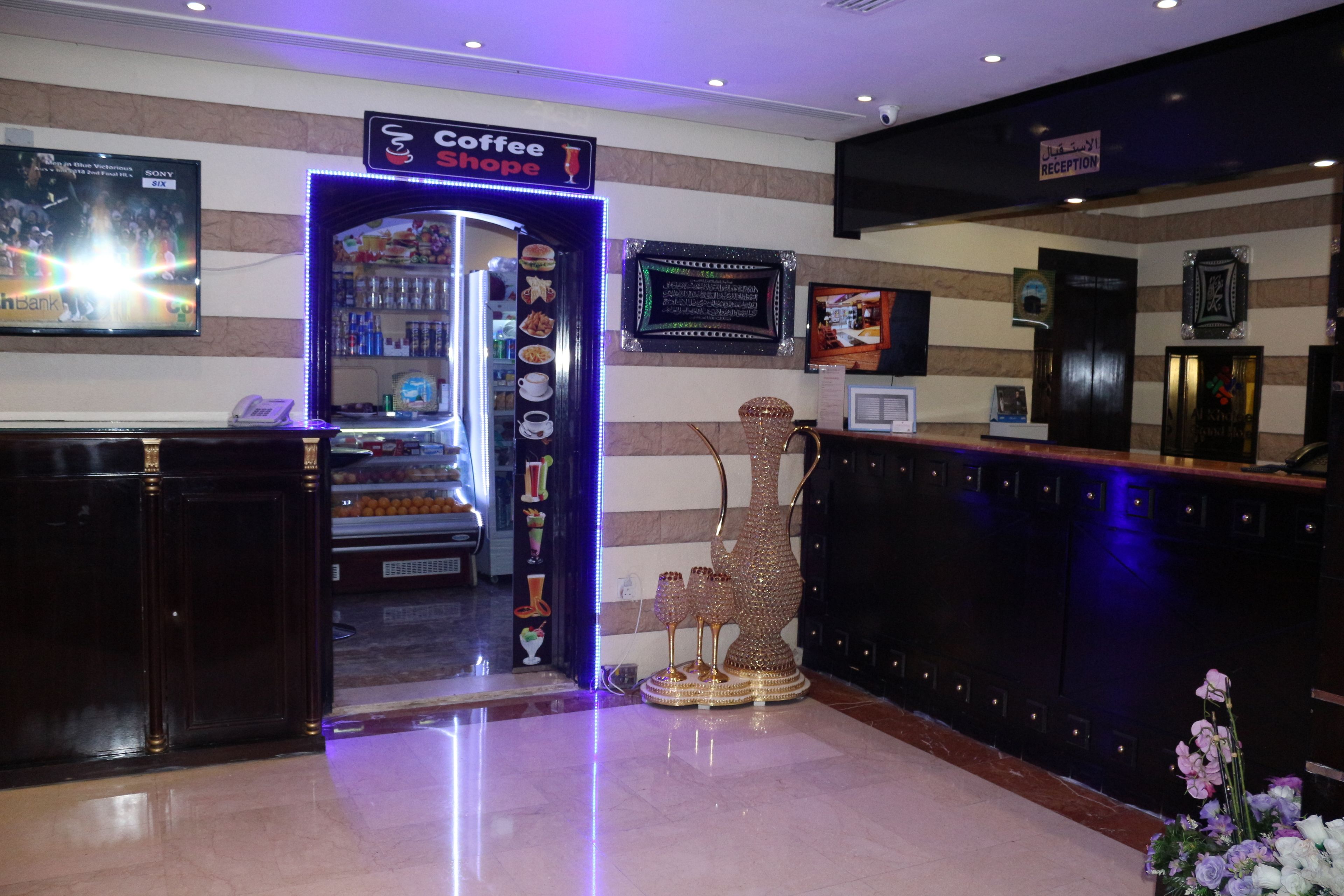 Un espace d’accueil d’hôtel comprenant un café, un comptoir de réception et un écran de télévision diffusant un film.