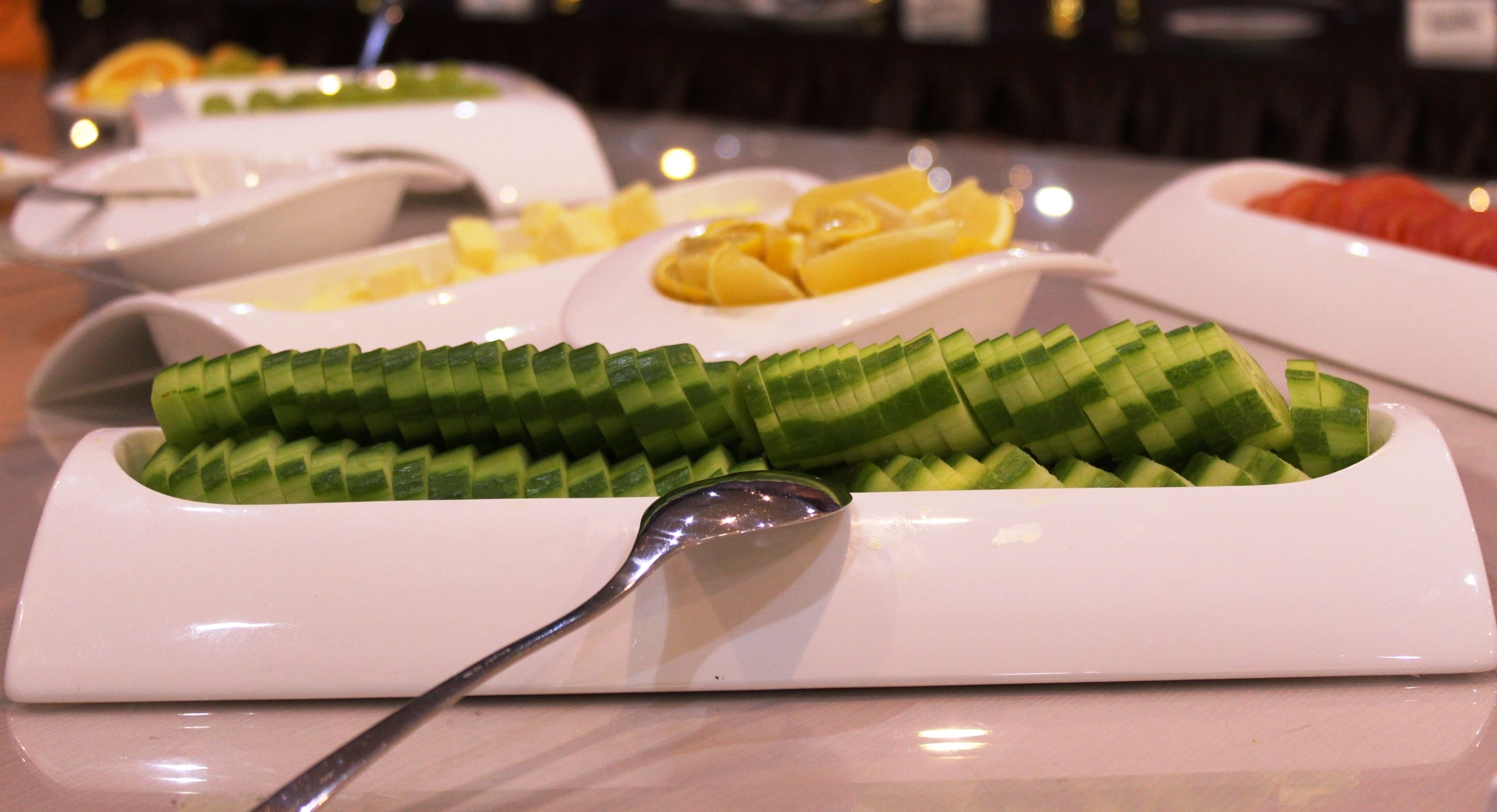 A buffet with various dishes, including a cucumber dish and a dish with yellow cubes.