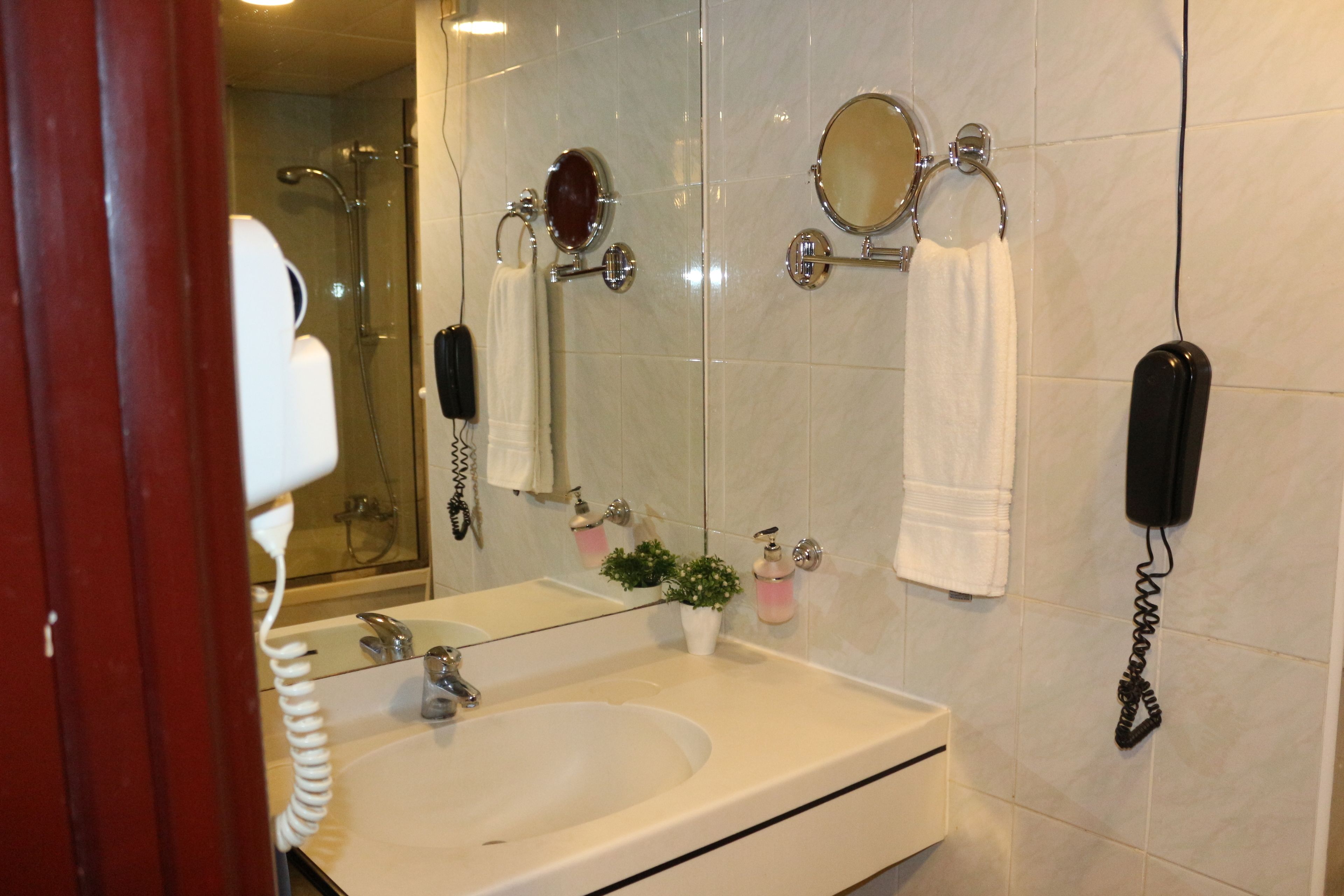 Een badkamer met een dubbele wastafel, een grote spiegel, twee ronde spiegels, een handdouche, een handföhn en een aan de muur bevestigd toestel.