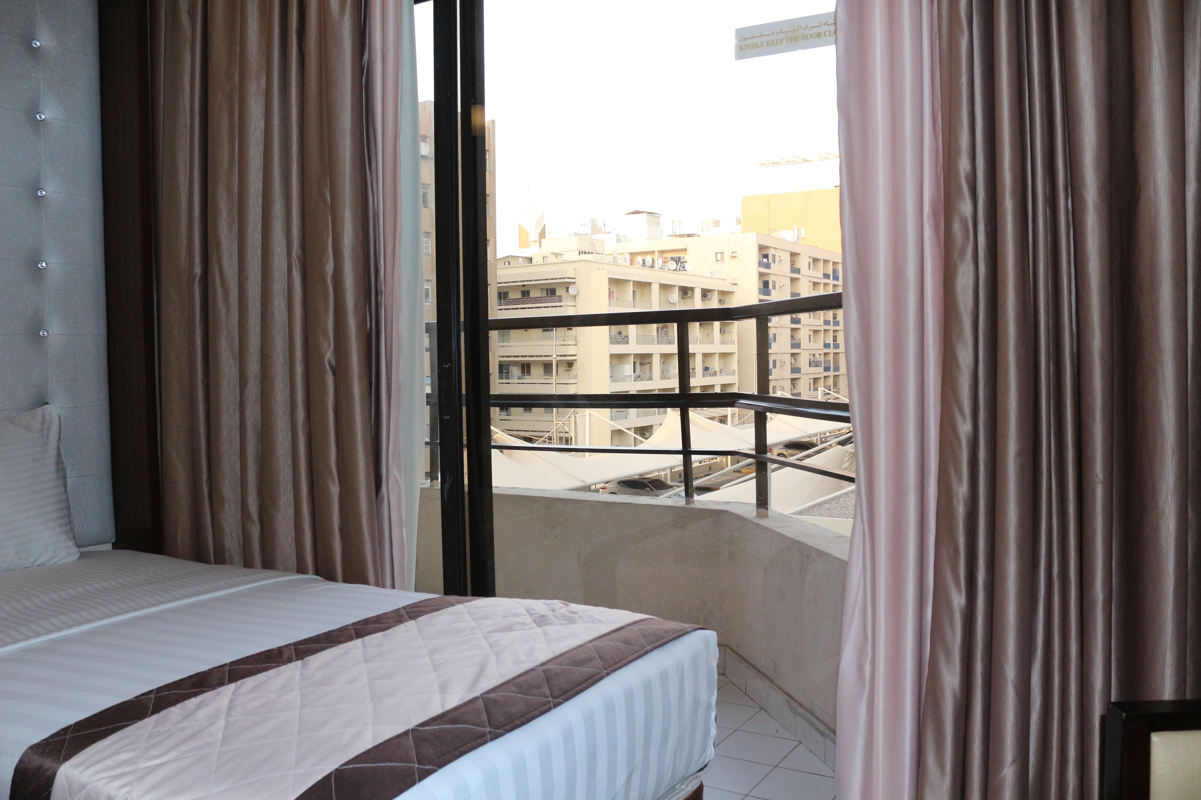 A hotel room with a bed, curtains, and a balcony with a view of buildings.