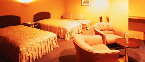Habitación de hotel con dos camas, un sofá, una mesita y una lámpara.
