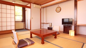 Une pièce de style japonais traditionnel, avec un sol recouvert de tatamis, une basse table en bois, un téléviseur et une porte coulissante.