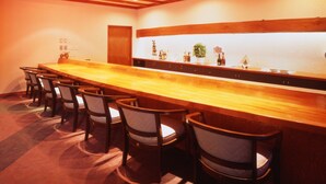 Un espace bar avec un long comptoir en bois, plusieurs chaises et un mur recouvert de carreaux blancs.