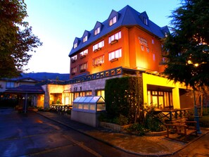 Un hotel de estilo arquitectónico europeo tradicional, con una entrada destacada que incluye una marquesina de cristal, un patio con asientos y una fachada bien iluminada.