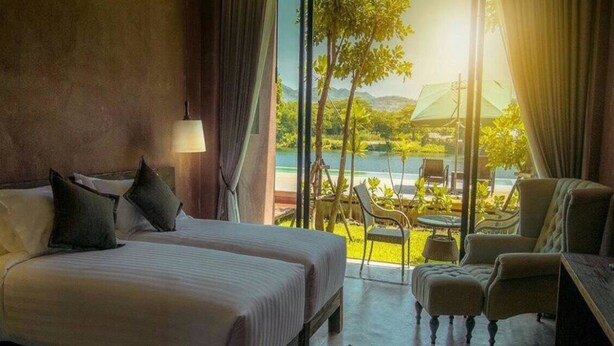 A hotel room with two beds, a sitting area with chairs, a view of a pool and greenery. - The Glory River Kwai Hotel (Kanchanaburi)