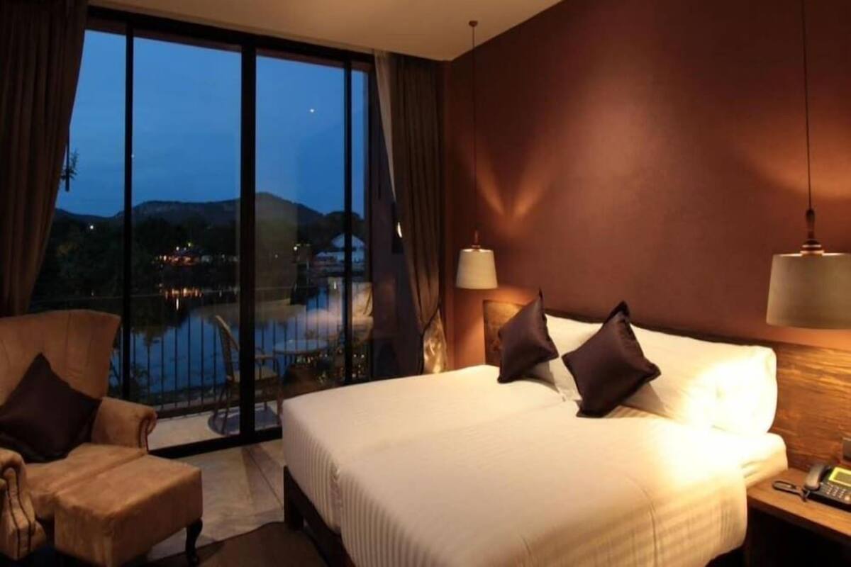 A hotel room with a large bed, a chair, a desk with a lamp, and a view of a pool and mountains.