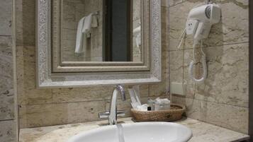 Une salle de bain avec un lavabo en marbre, un miroir doté d’un cadre orné, un sèche-cheveux fixé au mur et un panier en osier posé sur le comptoir.