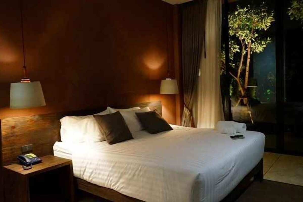 Habitación de hotel con una cama grande, dos lámparas de noche, una mesita de noche y vistas a un árbol a través de una ventana.
