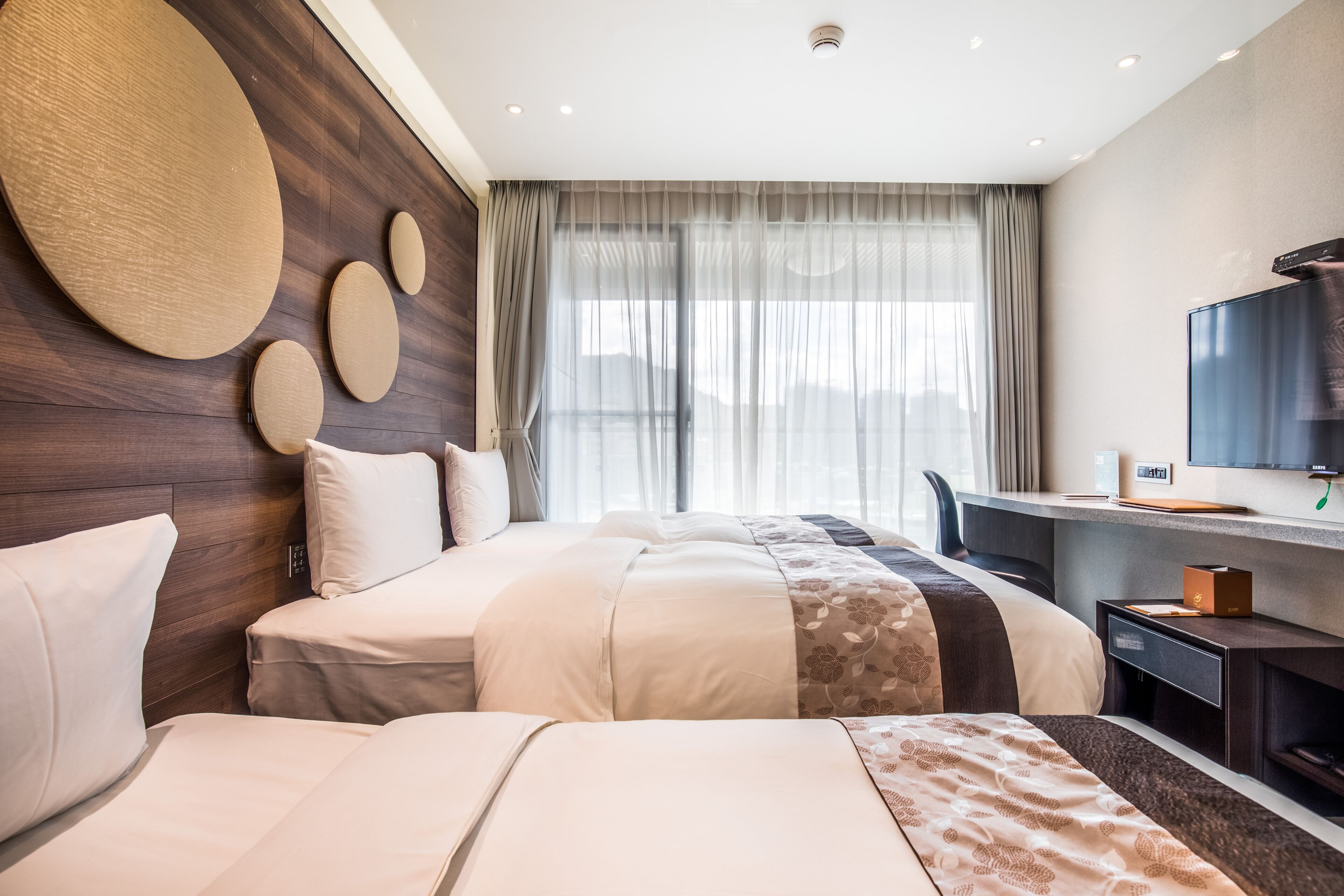 Hotelkamer met een groot bed, een bureau met een computer, een televisie en een groot raam met gordijnen.