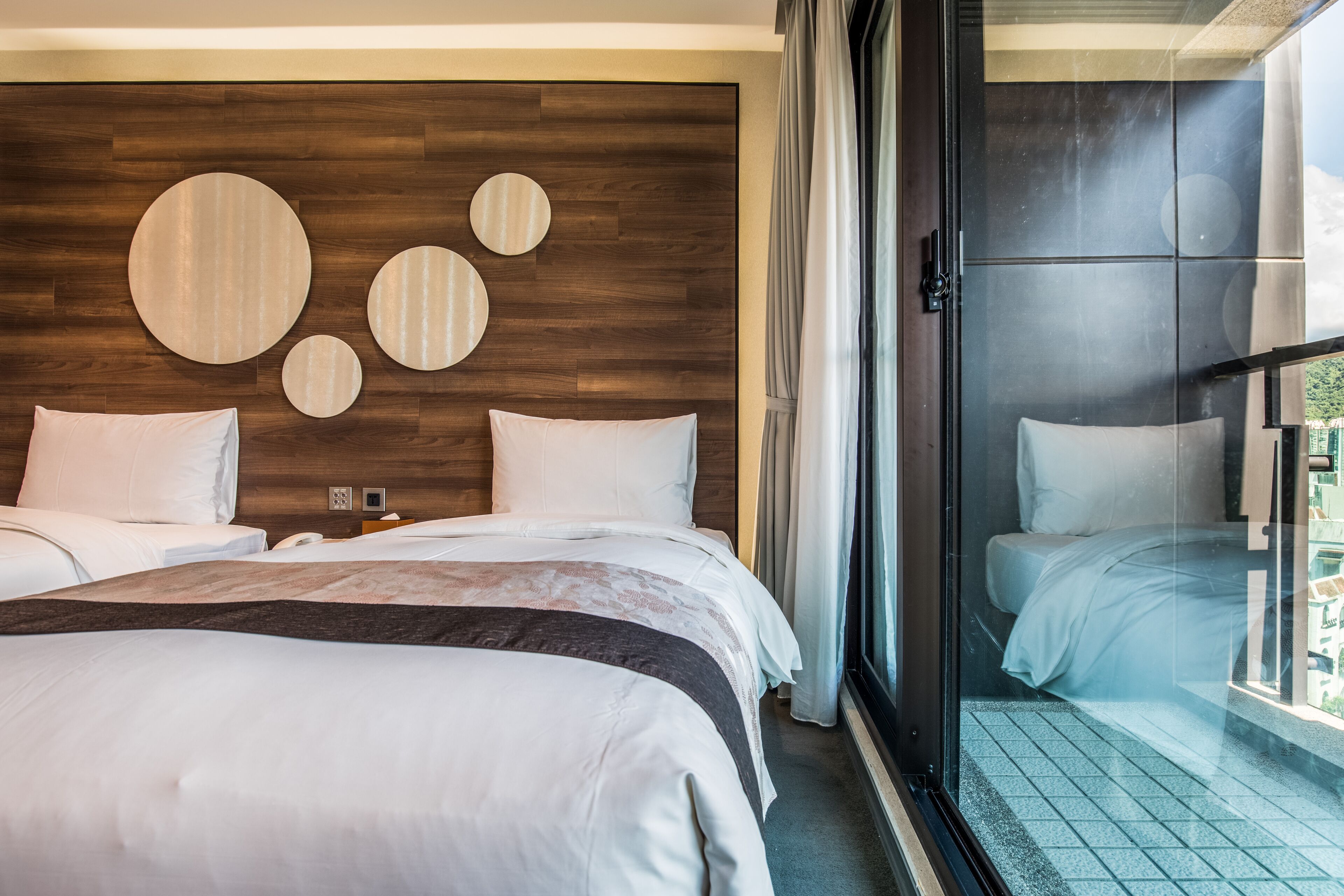 A hotel room with a large bed, a wooden headboard, and a view through a glass door.