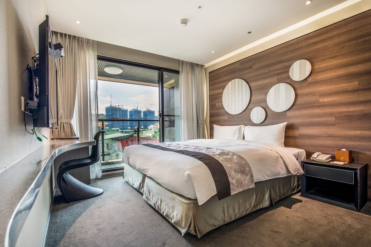 Ein modernes Hotelzimmer mit einem großen Bett, einem Schreibtisch, einem Fernseher und Blick auf die Stadt.